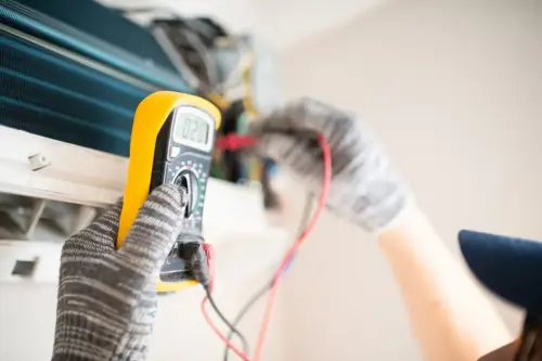 HVAC technician using a digital multimeter to diagnose and repair an indoor air conditioning unit.