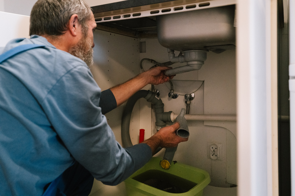Plumber repairing pipes under a kitchen sink, checking plumbing connections in Fort Calhoun, NE.